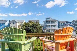 A deck with colorful Adirondack chairs, a wooden railing, and a view of houses in the background. - Pirates & Paradise: Private Pool, Home Theatre, and Pet Friendly (Surf City)