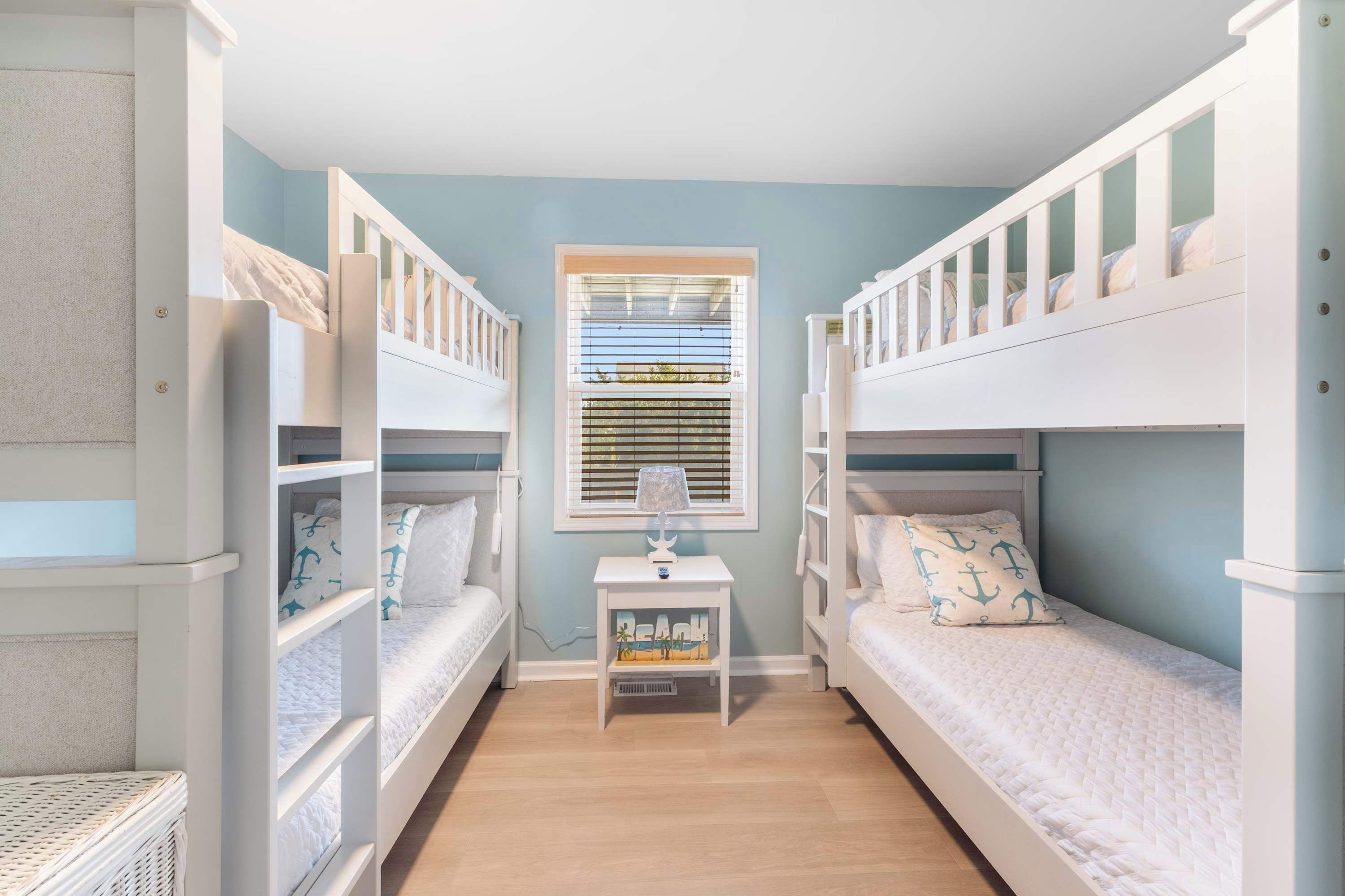 A children's room with bunk beds, a small table with a lamp, and a window with blinds.