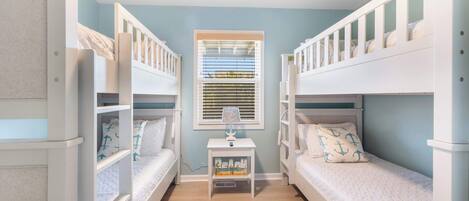 A children's room with bunk beds, a small table with a lamp, and a window with blinds.