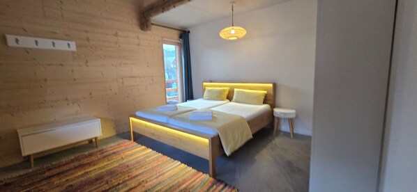 A bedroom with a bed, bedside table, bench, and a hanging light fixture.