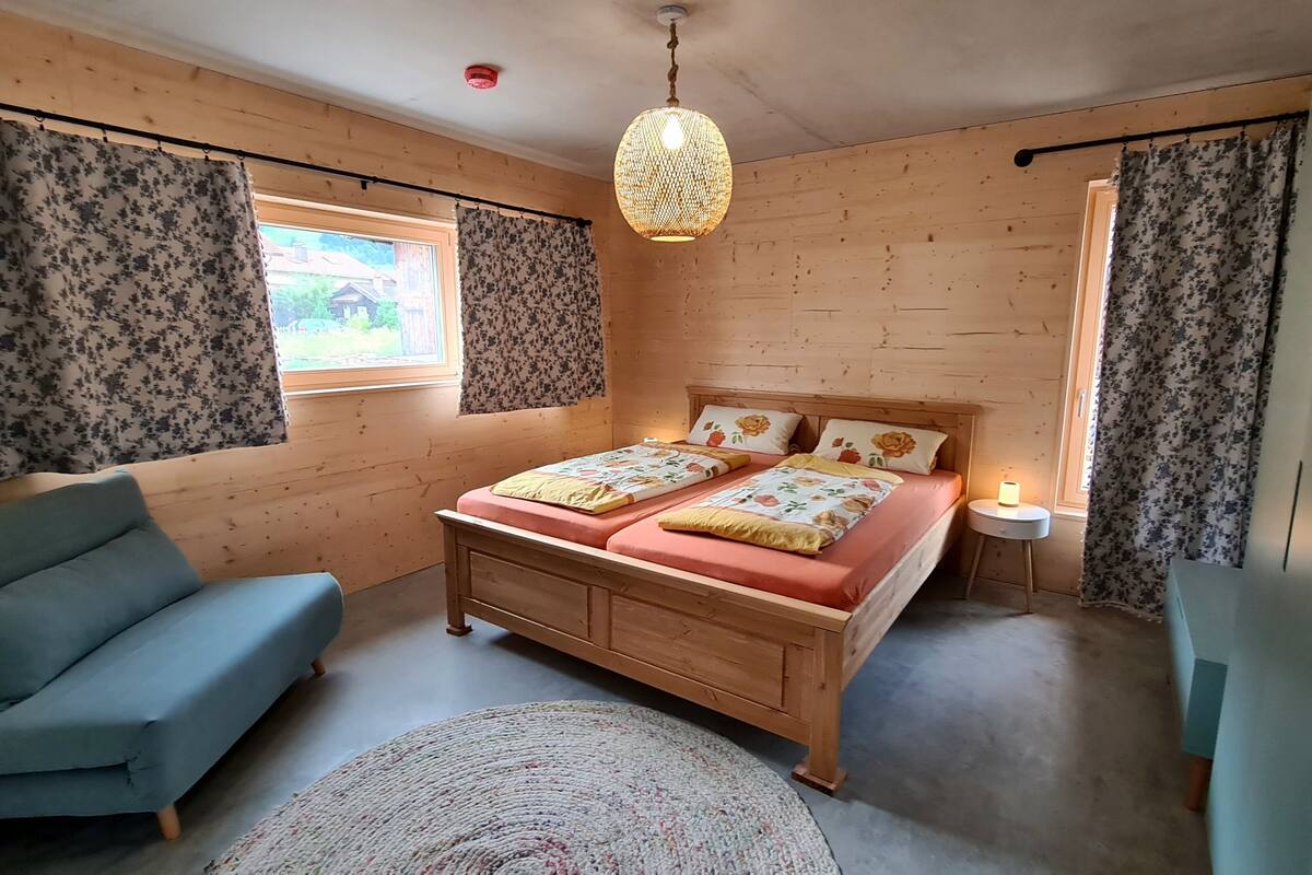 Une chambre à coucher avec un lit en bois, un canapé bleu, un tapis rond et une fenêtre avec des rideaux.
