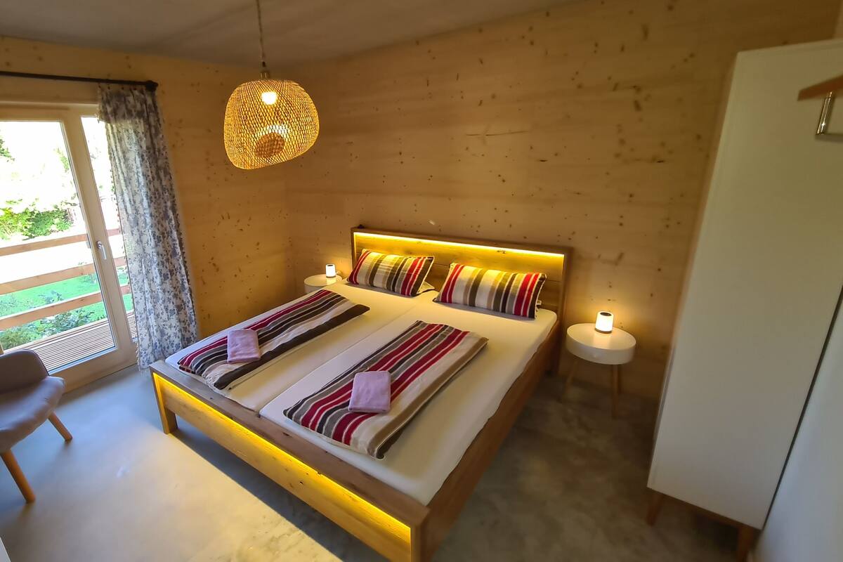 Une chambre à coucher comprenant un lit, des tables de chevet, une chaise, un luminaire suspendu et une vue sur l’extérieur.