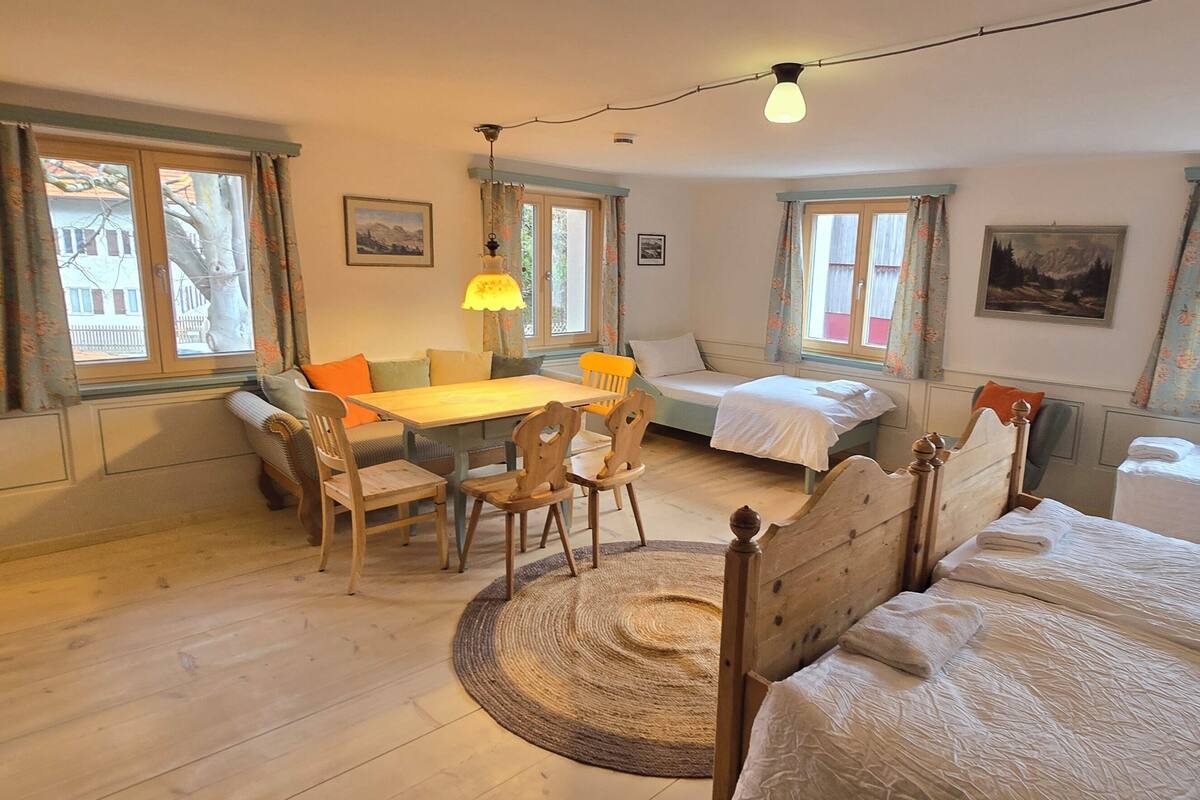 Une pièce confortable avec un lit en bois, une petite table avec des chaises, un canapé et une fenêtre avec des rideaux.
