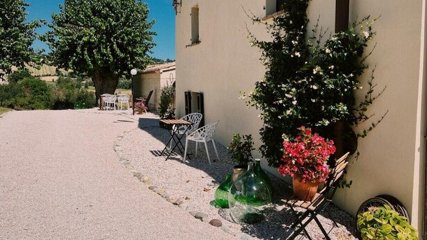 A building with a gravel courtyard, outdoor seating, and potted plants. - Casale Milleluci - apartment with a view of the hills 10 min from the sea (SENIGALLIA)