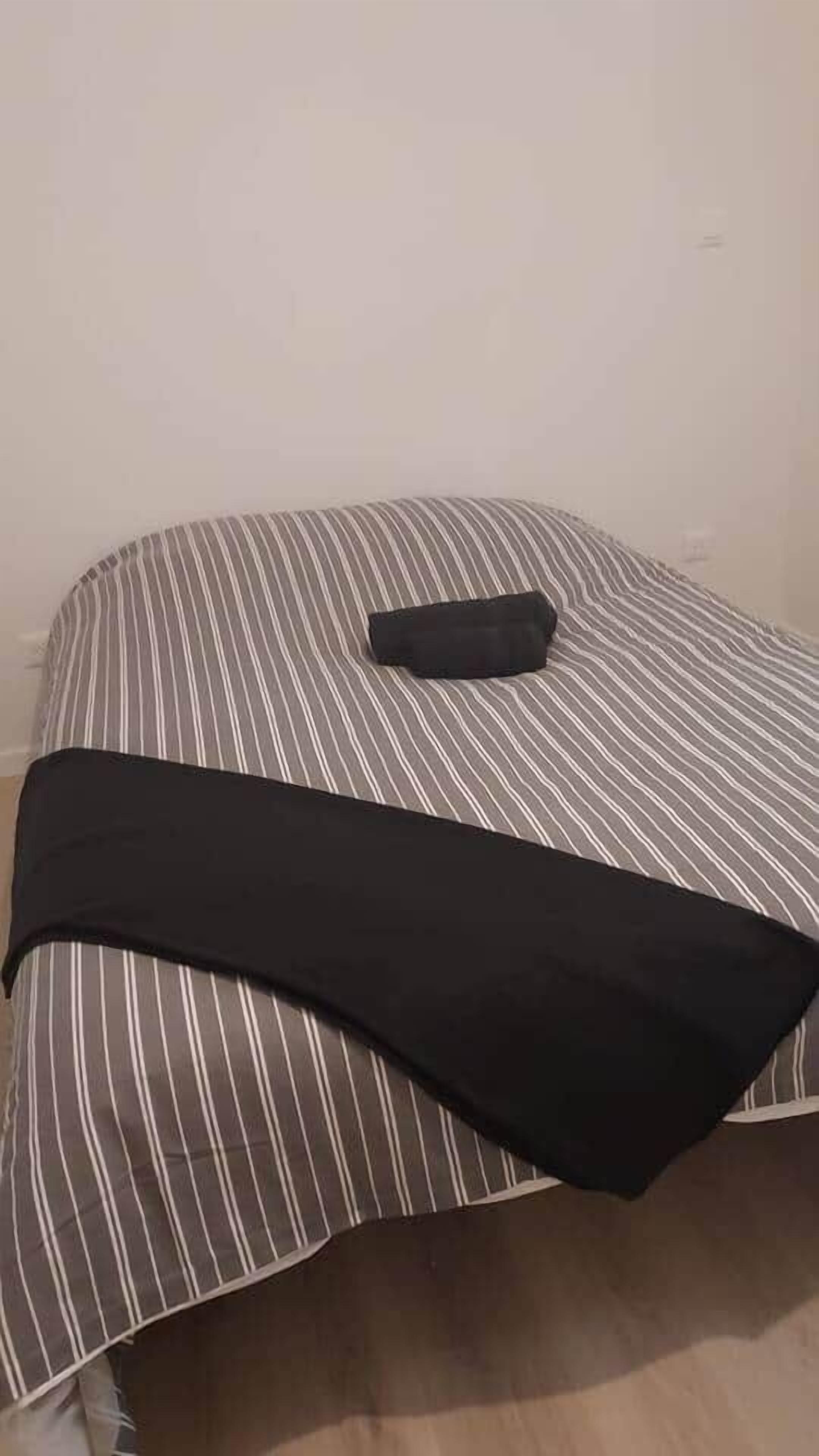A bed with a striped bedspread and a black blanket.