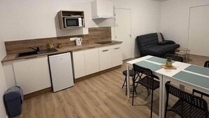 Een compacte keuken met een magnetron, een kleine koelkast, en een eethoek met een tafel en stoelen.