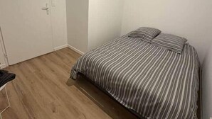 Een slaapkamer met een bed, houten vloeren, een deur en witte wanden.