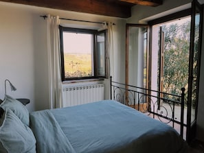 Ein Schlafzimmer mit einem Bett, einem Fenster mit Vorhängen, einer Heizung und Blick auf Grün.