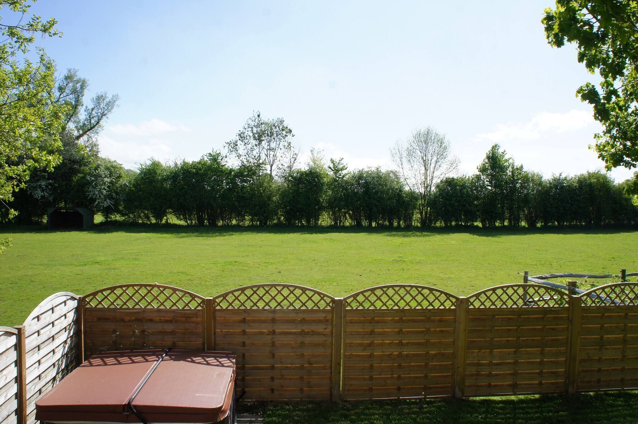 A fenced outdoor area with a lawn, a wooden gate, and a table with a red cover.