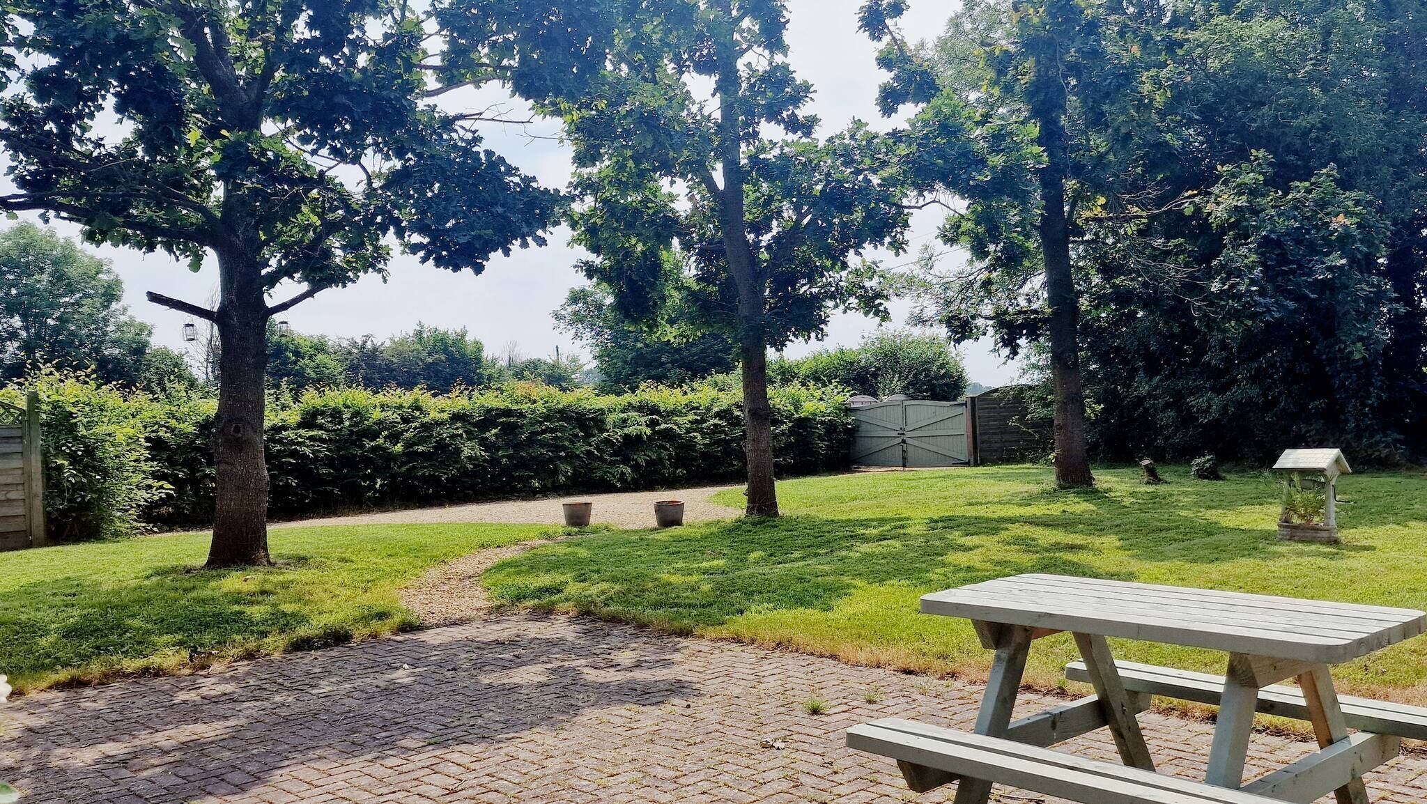 Ein Picknickplatz mit Tisch und Bänken, umgeben von Bäumen und einem Hecken.