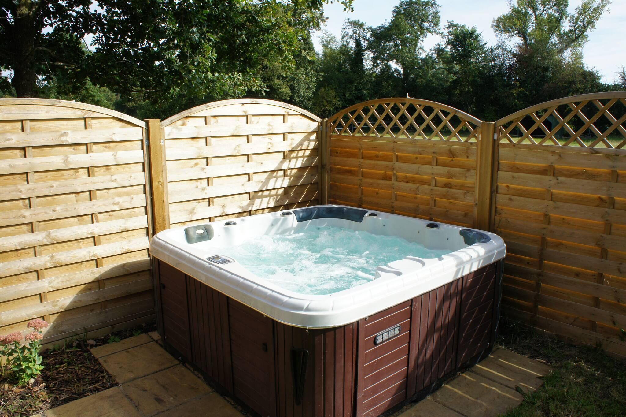 A hot tub in a backyard with wooden fencing and a wooden deck.