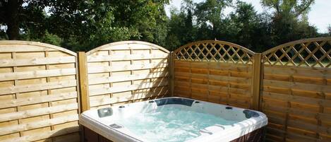 A hot tub in a backyard with wooden fencing and a wooden deck.