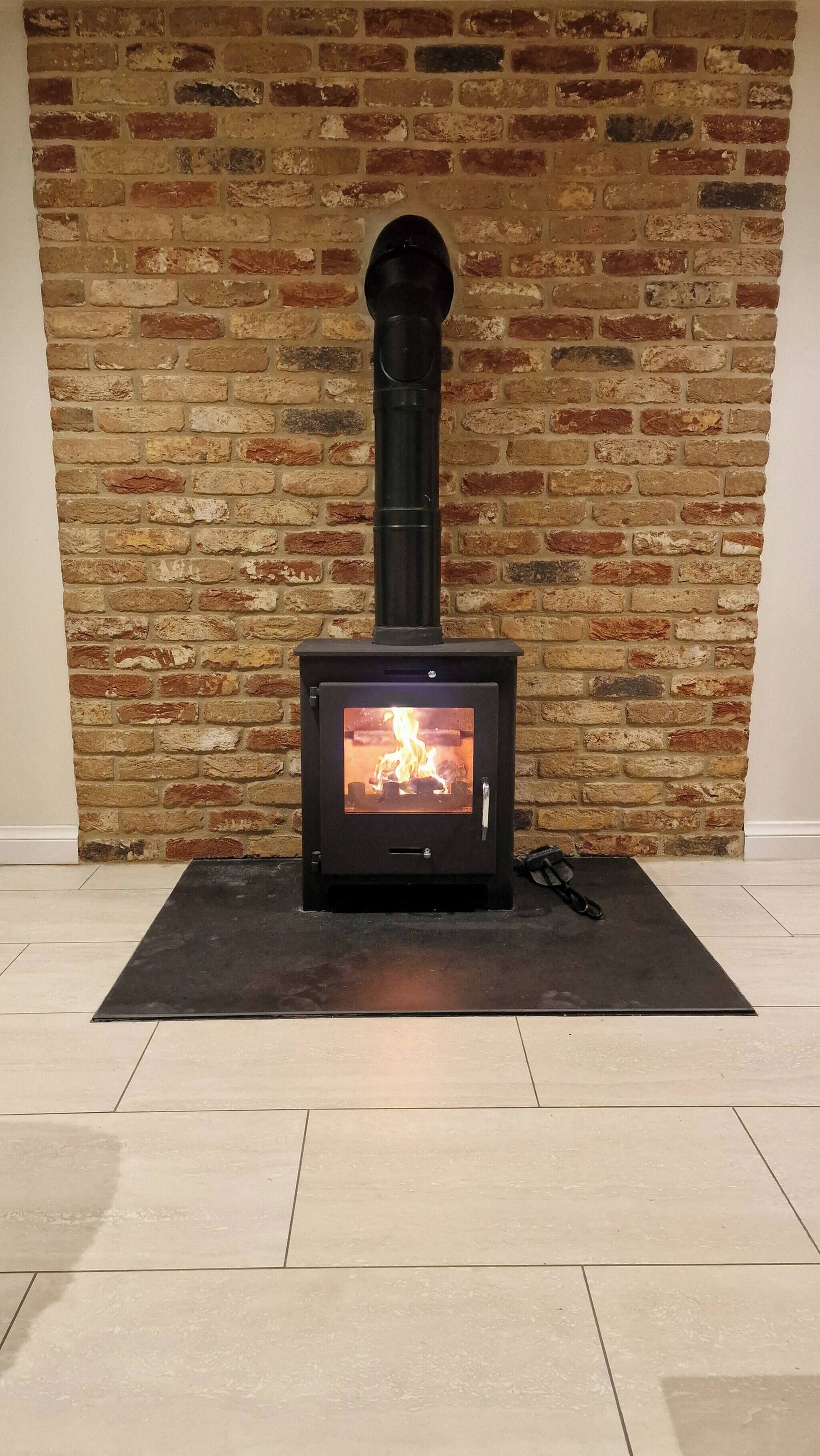 A wood-burning stove with a visible fire, set against a brick wall.