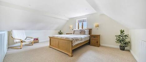 A bedroom with a sloped ceiling, a bed, a chair, bedside tables, and a potted plant.
