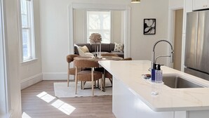 A modern kitchen with a large island, pendant lights, and a stainless steel refrigerator. - New 2BR/2BA LUXE Harvard & MIT w/Parking Red Line (Somerville)