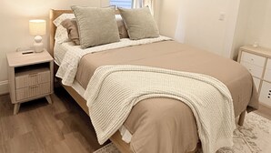 A bedroom with a bed, bedside tables, a window with curtains, and a wall-mounted picture. - New 2BR/2BA LUXE Harvard & MIT w/Parking Red Line (Somerville)
