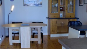 Une table de salle à manger en bois, accompagnée de chaises, un buffet aux portes vitrées et une petite table à la surface foncée.