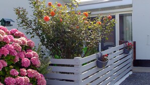 Une clôture en bois peinte en blanc, avec un jardinier contenant des fleurs orange et un arbuste à fleurs roses.