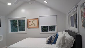A bedroom with a bed, two windows with blinds, a ceiling light, and a framed picture on the wall. - Serene 1-bedroom modern cottage in Keaau perfect for a relaxing getaway. (Keaau)