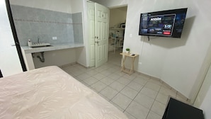 A bedroom with a bed, a small table, a TV mounted on the wall, and a bathroom with a sink and toilet. - Loft en Distrito Tec. a 5 min a Fundidora. Walmart Nuevo Sur, Seguro y caminable (Monterrey)
