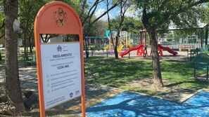 Un parc infantil amb un senyal que indica les normes d'ús, incloent un toc de queda a la mitjanit i prohibició d'abandonar llençorim.