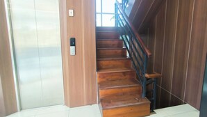 A wooden staircase with a handrail, a door with a light switch, and a window with natural light. - J&L Inn Semarang (Semarang)
