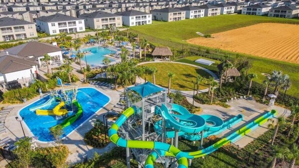 Vista aerea di un resort con una grande area piscina, scivoli acquatici e un quartiere residenziale sullo sfondo.