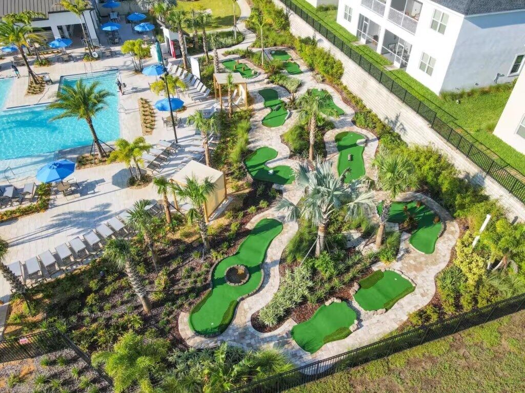 A golf course with multiple putting greens, a swimming pool, and lounge areas with umbrellas.
