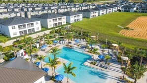 Un complesso residenziale con diversi edifici a due piani, una piscina centrale con lettini e una zona verde con palme.