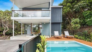 Ein modernes, zweistöckiges Haus mit Balkon, Schwimmbad und üppiger Bepflanzung.