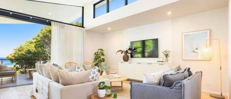 A modern living room with a sofa, armchairs, a TV, and a view of the sea.