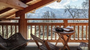 A wooden deck with a table and chairs, overlooking a mountainous landscape.