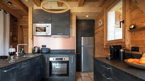 A modern kitchen with wooden walls, a built-in oven, a microwave, and a refrigerator.