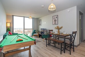 Een moderne woonkamer met een pooltafel, een eethoek en grote ramen met uitzicht op de stad.