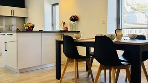 Ett modernt kök med matplats, med ett stort fönster, trägolv och en svart matstol.