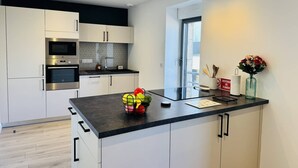 Ett modernt kök med vita skåp, en svart bänkskiva och vitvaror i rostfritt stål.