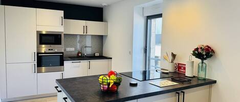 A modern kitchen with white cabinets, a black countertop, and stainless steel appliances.
