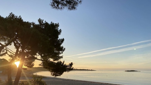 En strand med en klar himmel, en solnedgång och en avlägsen ö.