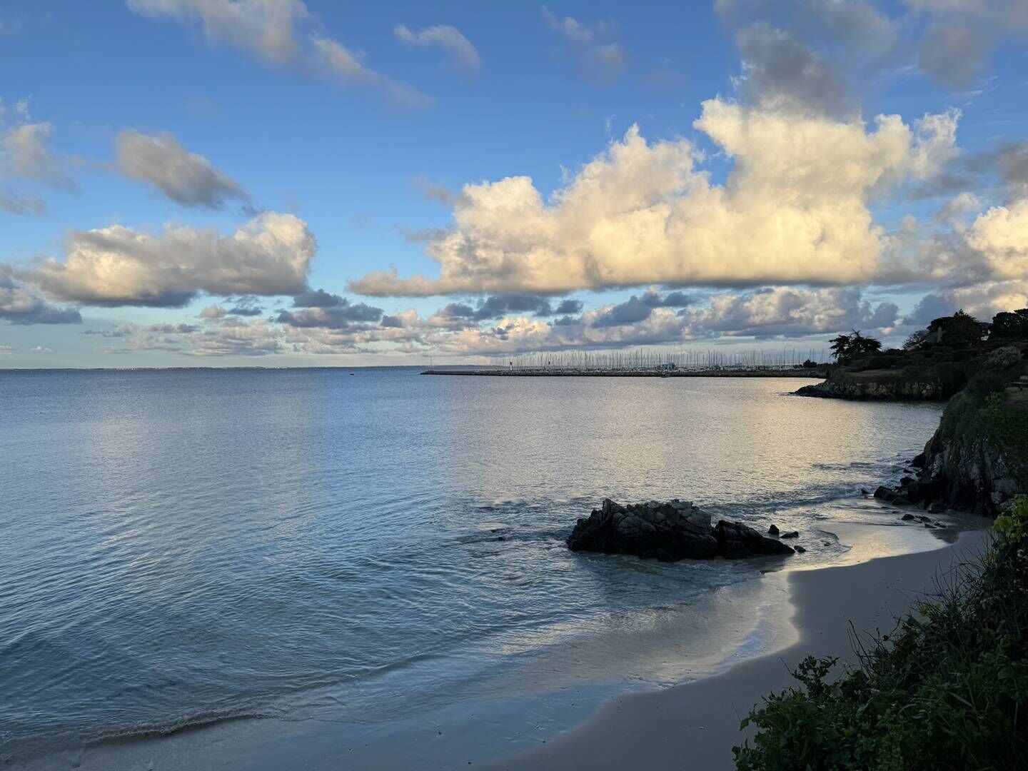 Et kystlandskab med et roligt hav, en sandstrand og en fjer borte bro.