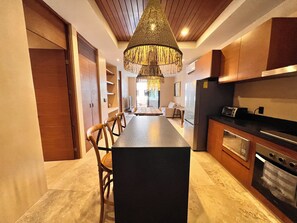A modern kitchen with a central island, wooden cabinets, and a hanging chandelier. - Elegant Dept Jacuzzi, Pool, GYM (Tulum)
