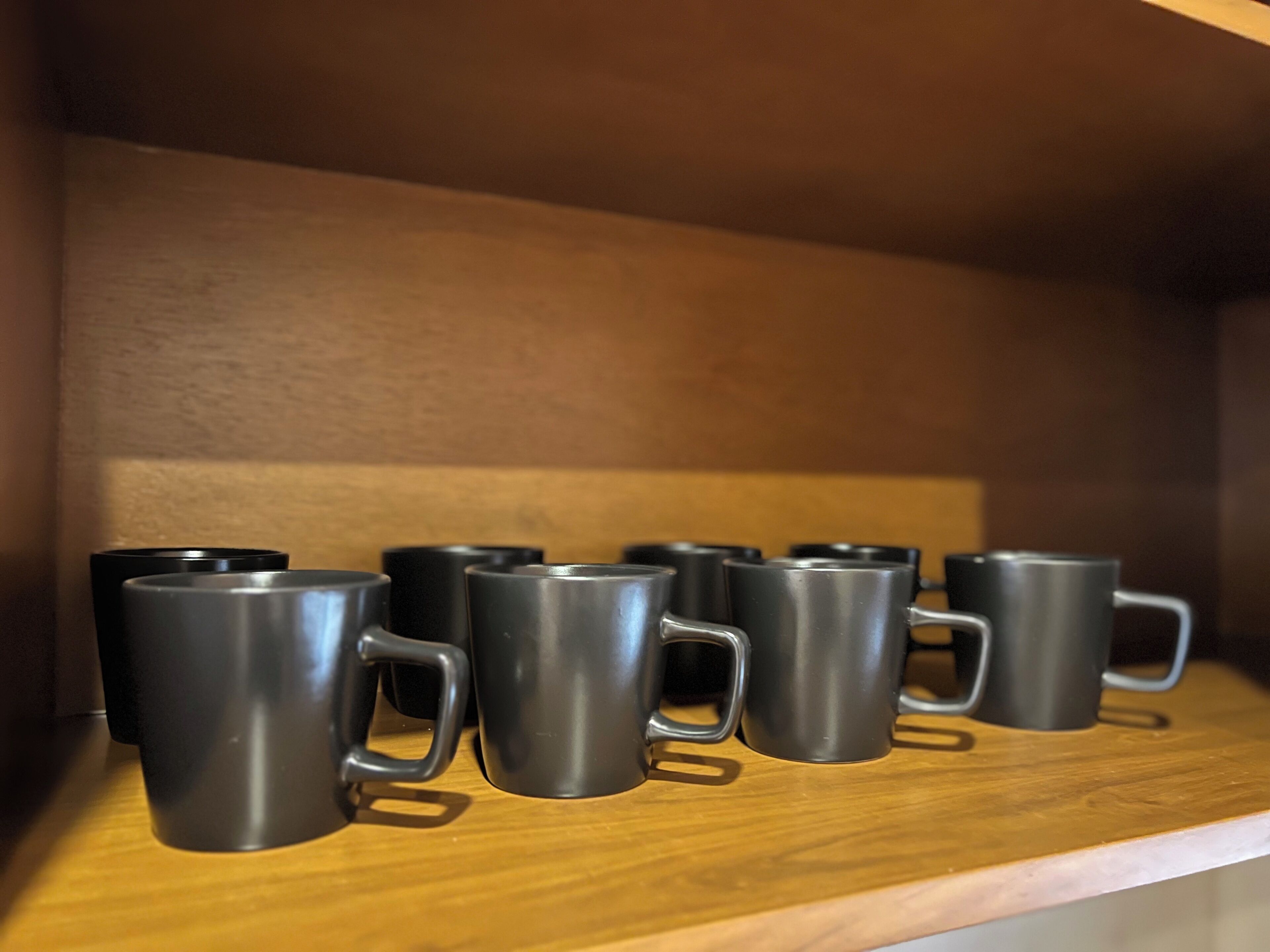 A shelf with several black mugs.