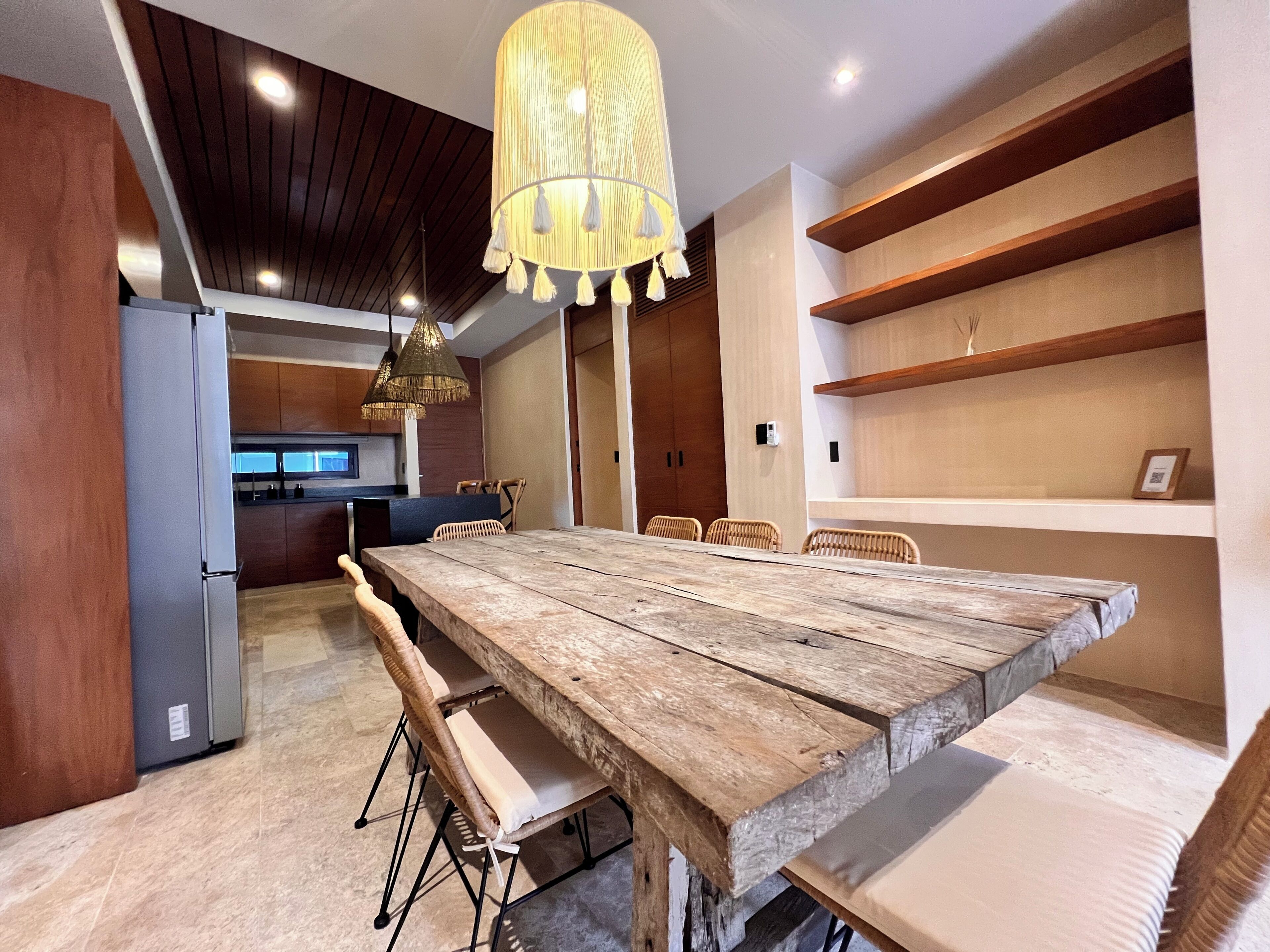 Un espace repas avec une grande table en bois, des chaises en osier et un luminaire suspendu.
