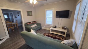 A living room with a sofa, a television, a small table, and a window. - New River Gorge Riverview Home in Meadow Creek.  3 bedroom, 1 bath, fenced yard (Meadow Creek)