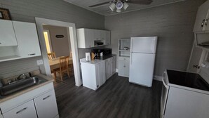 A compact kitchen with white cabinets, a refrigerator, a microwave, and a dining area with a table and chairs. - New River Gorge Riverview Home in Meadow Creek.  3 bedroom, 1 bath, fenced yard (Meadow Creek)