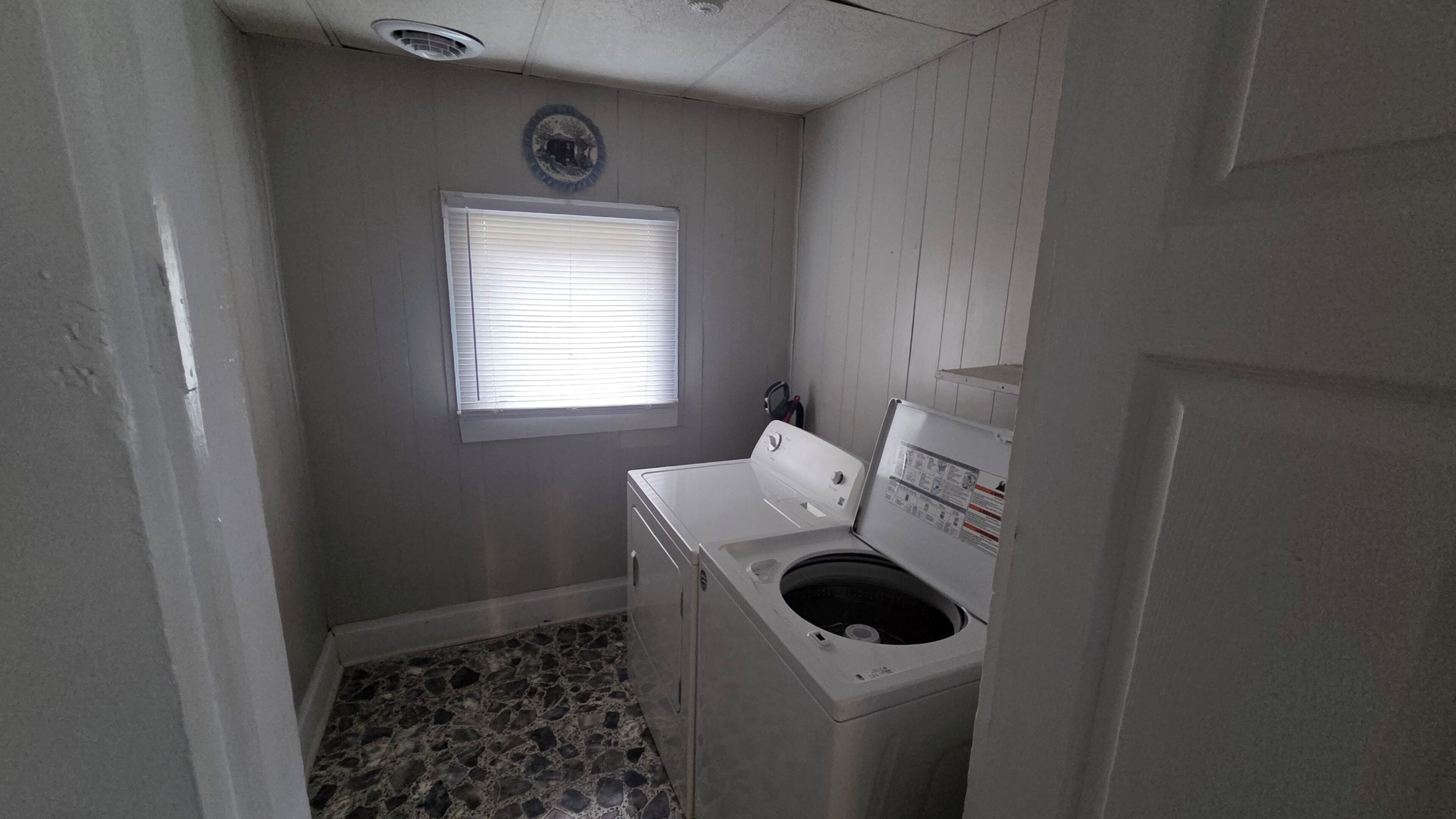 A laundry room with a washing machine, a small window, and a tiled floor.