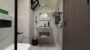 Ein modernes Badezimmer mit Marmorwaschbecken, einem Spiegel, einem Handtuchhalter und einem Mülleimer.