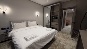 Ein modernes Hotelzimmer mit einem großen Bett, Nachttischlampen, einem Kleiderschrank und einem Schreibtisch mit Telefon.