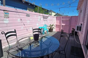 Eine Terrasse mit einem runden Glastisch, Metallstühlen, einem blauen Stuhl und einem rosafarbenen Zaun.