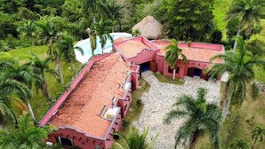 Un edificio de techo rojo con piscina, rodeado de palmeras y follaje.