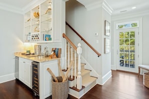 A kitchen with a built-in island, a wooden staircase, and a view through a glass door. - Luxury 6BR Golf Course Escape with Private Pool (Georgetown)